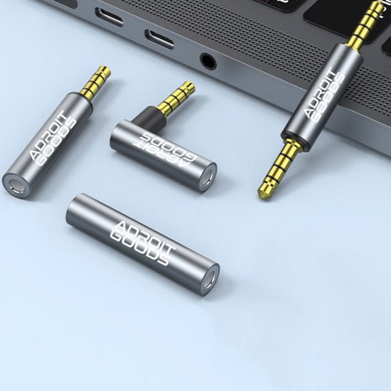 Grijze Adroit Goods audioadapters naast laptop met gouden connectors en 3,5 mm jackpluggen.