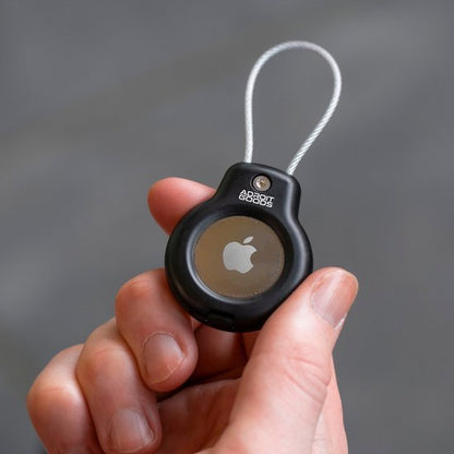 Hand houdt zwart beschermhoesje met een draadlus voor een ronde Apple tracker.