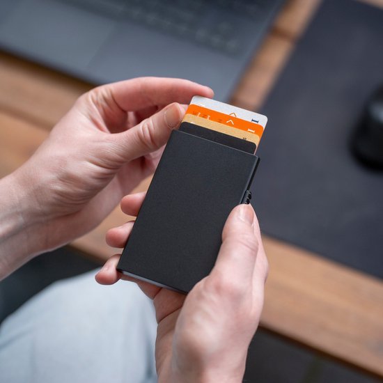 Handen houden een slanke zwarte portemonnee met meerdere kaarten zichtbaar aan de bovenkant vast