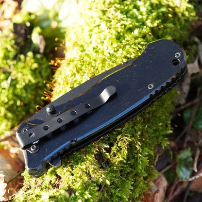gesloten zwart zakmes met metalen clip liggend op mos in de natuuromgeving