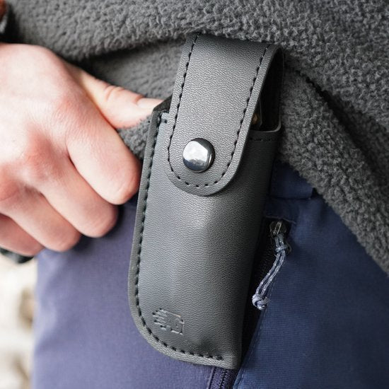 Hand die een zwarte leren hoes met drukknop aan een riem draagt, dicht bij een jas