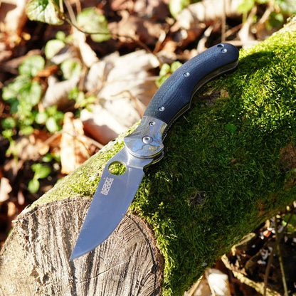 Opgevouwen zakmes met zwarte handgreep liggend op mosbedekt hout in de natuur