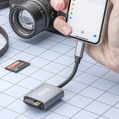 Hand verbindt smartphone met kaartlezer voor geheugenkaart naast camera op tafel