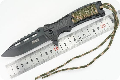 zwarte mes met gekarteld lemmet en camouflage koord naast metalen liniaal