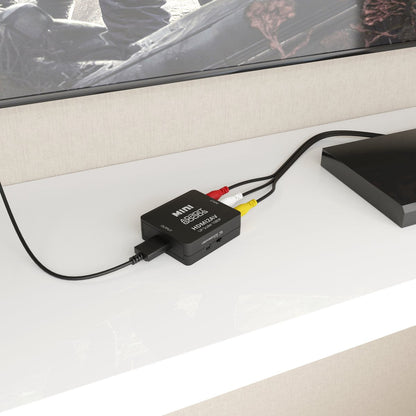 Kleine zwarte audio-video converter aangesloten met rode, witte en gele kabels op witte kast