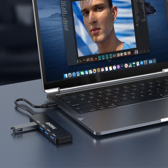 Close-up van een laptop met een zwarte USB-hub aangesloten op een grijze tafel.