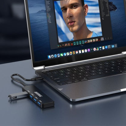 Close-up van een laptop met een zwarte USB-hub aangesloten op een grijze tafel.