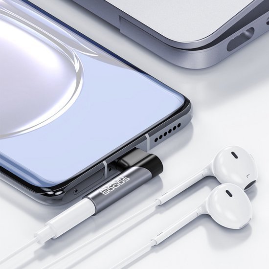 Smartphone met zwarte adapter en witte oordopjes op lichte ondergrond geplaatst