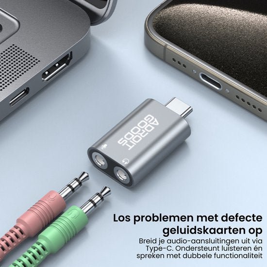 kleine grijze adapter met dubbele audiopoorten naast laptop en smartphone