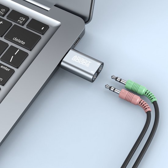 Adapter met AdroitGoods-logo aangesloten op laptop naast groene en roze audiokabels
