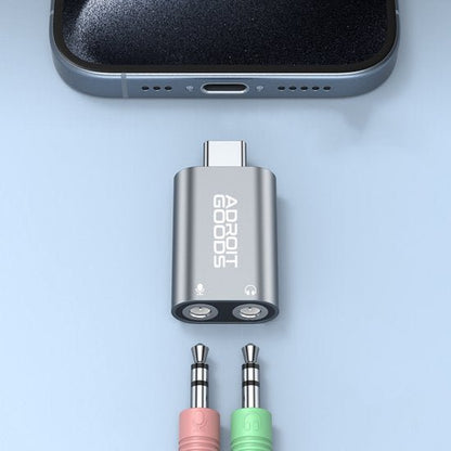 Zilverkleurige AdroitGoods USB-C adapter met twee 3,5 mm audiopoorten naast smartphone poort