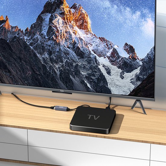Moderne televisie met berglandschap op scherm en aangesloten zwart streamingapparaat op houten plank
