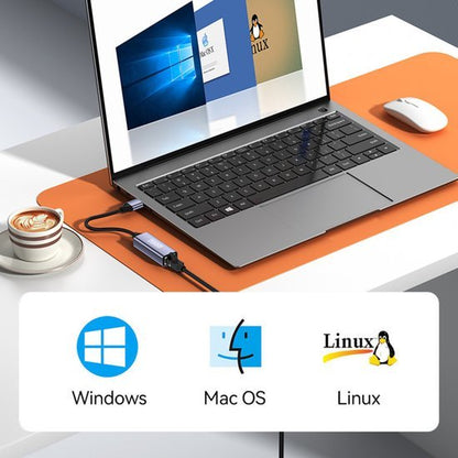 Laptop met adapter op oranje mat, scherm toont Windows, Mac OS en Linux besturingssystemen