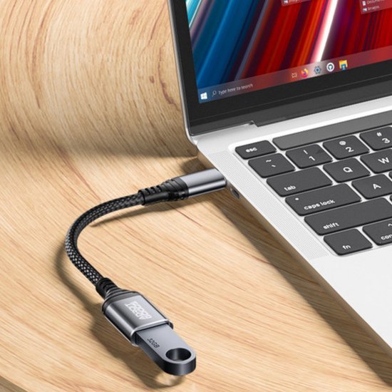 USB-stick met metalen behuizing en gevlochten kabel aangesloten op laptop in natuurlijke omgeving