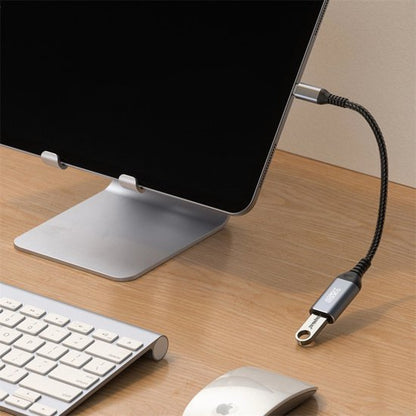 Een zwarte flexibele kabel met metalen connector aan een scherm bevestigd op een houten bureau.