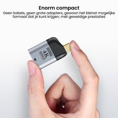 Hand die een kleine zilveren compacte adapter met gouden aansluiting vasthoudt tegen een witte achtergrond