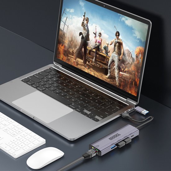 Laptop met open beeldscherm waarop een actiespel speelt, aangesloten op meerdere externe apparaten.